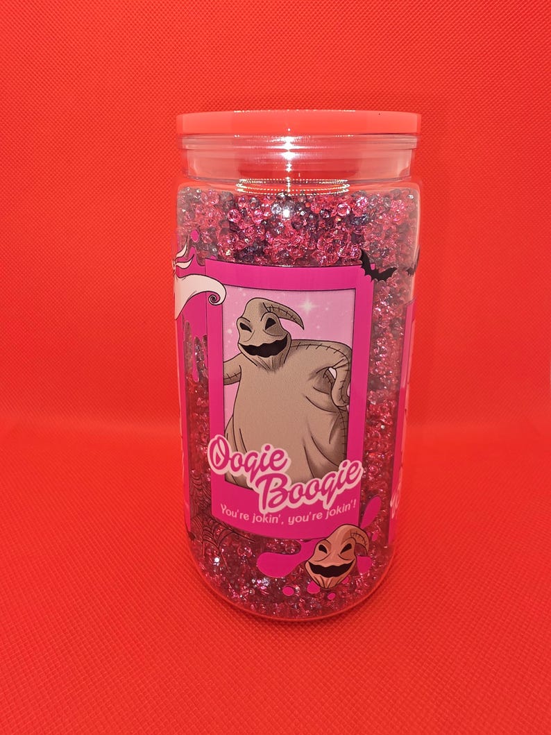 K&ouml;nnte beinhalten: Ein durchsichtiges Plastikglas gef&uuml;llt mit rosa Glitzer und einem rosa Deckel. Das Glas hat ein rosa Etikett mit einer Illustration von Oogie Boogie aus The Nightmare Before Christmas, mit dem Text "Oogie Boogie" und "You're jokin', you're jokin'!"