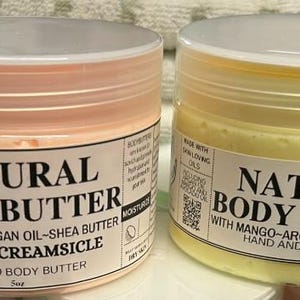May include: Two jars of natural body butter. One is orange creamsicle-scented, the other is mango-scented. Each jar has a white label with black text that reads "Natural Body Butter" and the ingredients. The jars are 5 oz.