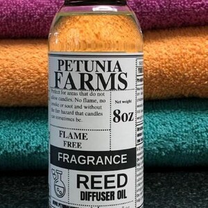 May include: A clear plastic bottle with a black cap containing Petunia Farms fragrance reed diffuser oil. The white label features black text, including the brand name, the phrase Flame Free, and a net weight of 8oz, with a small beaker icon.