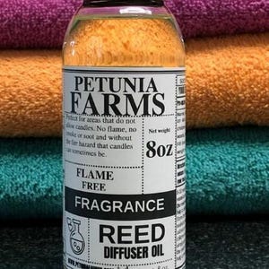 May include: A clear plastic bottle with a black cap containing Petunia Farms fragrance reed diffuser oil. The white label features black text, including the brand name, the phrase Flame Free, and a net weight of 8oz, with a small beaker icon.