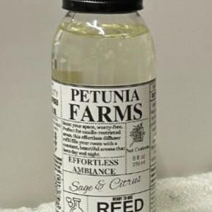 May include: A clear plastic bottle filled with light yellow reed diffuser oil, topped with a black screw cap. The white label features the text Petunia Farms, Effortless Ambiance, Sage & Citrus, and Reed Diffuser Oil, with a net content of 8 fl oz.