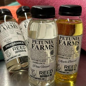May include: Four clear plastic bottles of Petunia Farms reed diffuser oil with black screw-top lids. Each bottle features a white label with black text, including the brand name, product type, and a net content of 8 fl oz or 236 ml.