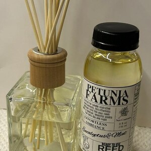May include: A square glass reed diffuser bottle with a wooden collar and light-colored reeds, paired with a plastic bottle of Petunia Farms Eucalyptus & Mint reed diffuser oil, labeled 8 fl oz, 236 ml, and Ready to Use Reed Diffuser Oil.