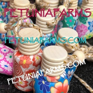 May include: A collection of small, colorful, floral patterned glass bottles with wooden stoppers and gold string. The bottles are hanging from the string and have the text "PETUNIAFARMS.COM" on them.