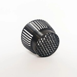 May include: A black, cylindrical object with a lattice design. The top section has vertical slits, and the bottom has a honeycomb pattern. The object is set against a white background, highlighting its intricate structure.