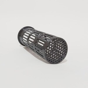 May include: A black, cylindrical object with a cage-like structure. The design features vertical and horizontal openings, forming a grid. The ends of the cylinder have a solid, textured surface with small holes. It appears to be a filter or a container of some kind.