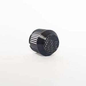 May include: A black, cylindrical object with a perforated, honeycomb-like surface on one end and a series of parallel slits on the sides. The object appears to be made of plastic or a similar material and is set against a white background.