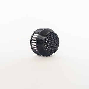 May include: A black plastic drain cover with a circular shape. The cover has a grid-like pattern on the top and vertical slits around the sides. The object is set against a white background.