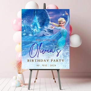 May include: A rectangular birthday party welcome sign featuring a blonde character in a blue dress, an ice castle, and snowy background. The text reads: WELCOME TO Olivia's BIRTHDAY PARTY 10 MAY 2024. The sign is displayed on a black easel stand.