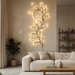 May include: A decorative wall-mounted light fixture shaped like a tree branch with warm white lights. The fixture is mounted on a neutral-colored wall above a cream-colored sofa. A potted plant and wooden coffee table complete the scene.