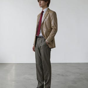 May include: A tan leather blazer with a red tie, white dress shirt, and gray trousers. The outfit is completed with a black belt. The ensemble is a classic business casual style.