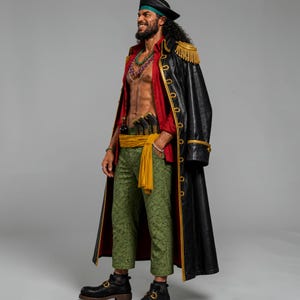 May include: A person in a pirate costume, wearing a black coat with gold trim and epaulets, a red shirt, and green patterned pants. The costume includes a black hat, a yellow sash, and black boots. The person is smiling.