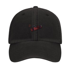 Puede incluir: Gorra de béisbol negra con un diseño bordado de dinamita en rojo y azul. La gorra tiene una visera curva y una correa ajustable. La dinamita tiene una mecha encendida.