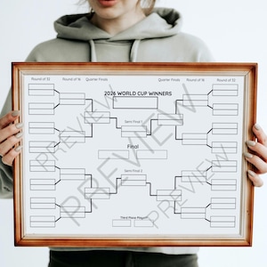 May include: A framed bracket chart for the 2026 World Cup Winners, featuring a wooden frame. The chart is white with black lines and text, including "Round of 32", "Round of 16", "Quarter Finals", "Semi Final 1", "Final", "Semi Final 2", and "Third Place Playoff".