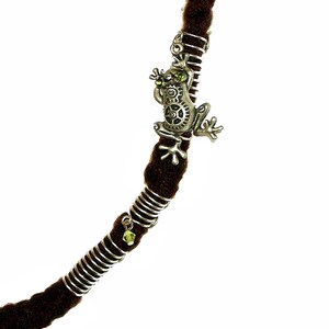 May include: A brown dreadlock with a silver metal frog charm and a green crystal bead. The frog has a gear design and is holding a green crystal bead in its mouth.