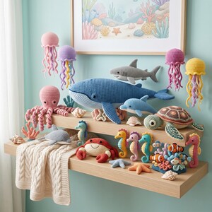 May include: A collection of handmade crochet sea creatures, including a blue whale, dolphins, sharks, jellyfish, seahorses, and a crab, arranged on a wooden shelf. The shelf also holds a cream-colored cable-knit blanket and decorative seashells. A framed ocean-themed artwork hangs in the background.