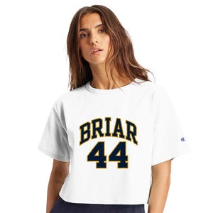 Puede incluir: Una camiseta blanca corta de manga corta con el texto BRIAR en una fuente arqueada de color azul oscuro sobre el número 44 en una fuente azul oscuro a juego. Un pequeño logotipo de Champion es visible en la manga izquierda.