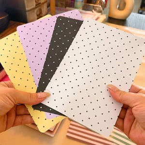 Peut inclure: Un ensemble de quatre cartes rectangulaires présentant un motif à pois. Les cartes sont de couleur jaune, violet clair, noir et blanc, chacune avec de petits points blancs ou noirs disposés en grille régulière sur la surface du papier.