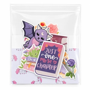 Puede incluir: Una colección de pegatinas de vinilo en una bolsa de plástico transparente con un murciélago morado, un dragón verde, un libro rosa con el texto JUST one more chapter, una rosa morada y elementos florales sobre un fondo de unicornios lila.