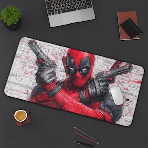 May include: A rectangular desk mat featuring a detailed illustration of Deadpool in a dynamic pose, holding two guns. The artwork is predominantly red and black, with a white background and technical drawing elements. A computer mouse is visible.