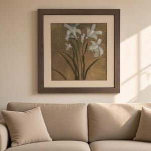 May include: A square framed wall art piece featuring a botanical illustration of white iris flowers with long dark green stems against a textured metallic gold background, enclosed in a dark brown wooden frame with a wide cream-colored mat board.