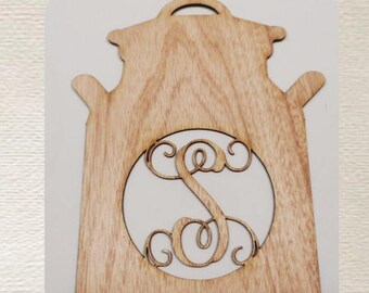 May include: Wooden milk jug-shaped sign with a light wood grain finish. A circular cutout reveals a white background with a decorative letter "S". The sign has a handle at the top and two side handles.