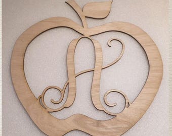 May include: Wooden apple-shaped cutout with a decorative letter A in the center. The apple is a light brown color and has a stem and leaf.