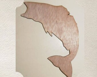 May include: A wooden cutout of a fish, with a light brown stain. The fish is facing to the right and has a large tail fin. The cutout is on a white background.