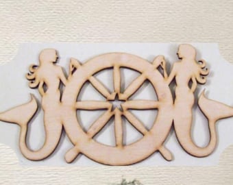 May include: Wooden nautical-themed cutout featuring a ship's wheel flanked by two mermaid silhouettes. The wheel has multiple spokes and a star-shaped center. The mermaids have flowing hair and fishtails. A nest with eggs is at the bottom.