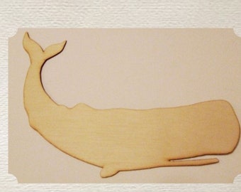 May include: A wooden whale cutout, painted in a light brown color, is lying on a light brown surface. The whale is facing the right side of the image. The whale has a rounded body and a long, thin tail.