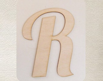 May include: A wooden letter R in a cursive font. The letter is cut out of a light brown piece of wood and is about 6 inches tall.