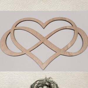 May include: A wooden cutout of an infinity symbol intertwined with a heart shape. The cutout is light brown and has a smooth finish.