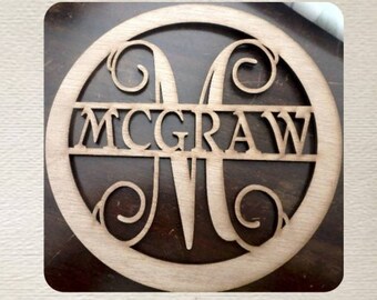 May include: A wooden monogram with the letter "M" and the name "MCGRAW" cut out in a circular design. The wood has a natural, light brown color. The design is set against a dark brown background.