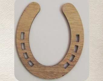 May include: A wooden horseshoe with rectangular cutouts, set against a white background. Below the horseshoe is a detailed illustration of a bird's nest with eggs and floral accents. The horseshoe is a light brown color.