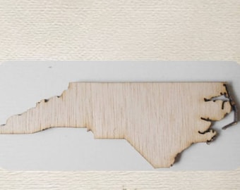 May include: A wooden cutout of the state of North Carolina. The cutout is a light brown color and has a smooth surface.