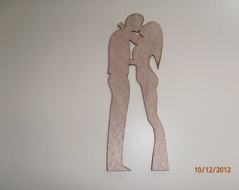 May include: A wooden silhouette of a couple kissing. The figures are cut from light-colored wood, with the man in a suit and the woman with long hair. The piece is a decorative item, likely for a wall or shelf.
