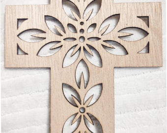 May include: Wooden cross with a floral design cut out of the center. The cross is made of light-colored wood and has a natural finish. The floral design is symmetrical and adds a decorative element.