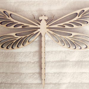 May include: A wooden dragonfly cutout with intricate details. The dragonfly is light brown and has a delicate, lacy design.