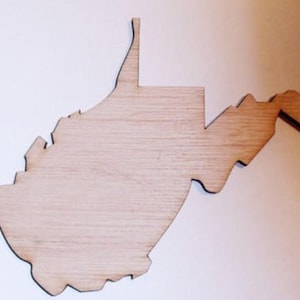 May include: A wooden cutout of the state of West Virginia. The cutout is made of light brown wood and has a smooth, unfinished surface.