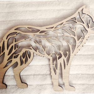 May include: A wooden wolf silhouette with a detailed design of branches and leaves cut out of the wood. The wolf is standing on all four legs with its head turned to the side.