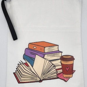 May include: A white zippered pouch with a black wrist strap featuring a printed illustration of a stack of books, an open book, and a coffee cup with a heart design. The books are orange, purple, and blue, while the coffee cup is brown and red.