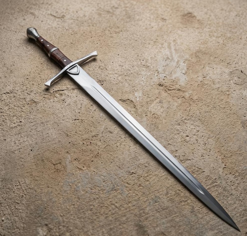 May include: A long, silver sword with a polished blade and a brown wooden handle. The sword features a crossguard and a rounded pommel. The blade is approximately 36 inches long.