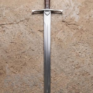 May include: A long, silver sword with a brown handle and a crossguard. The blade is straight and tapers to a point. The sword is set against a textured, tan background.