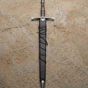 May include: A medieval sword with a silver crossguard and a brown handle. The sword is sheathed in a black leather scabbard, wrapped with leather strips. The tip of the scabbard is silver.