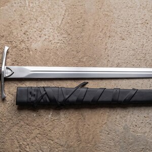 May include: A medieval sword with a polished steel blade and a wooden handle. The sword is laid out next to its black leather sheath. The handle is a dark brown color, and the crossguard is silver.