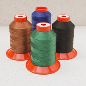 May include: Four spools of thread in brown, blue, green, and black. Each spool is on a red base with a red top. The thread is tightly wound, and the spools are arranged on a white surface.