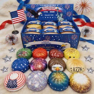 Puede incluir: Una caja de Liberty Dumplings con temática patriótica, con una bandera estadounidense, fuegos artificiales y la Estatua de la Libertad. Las empanadillas están decoradas con varios diseños, incluyendo estrellas, rayas y el número "250".