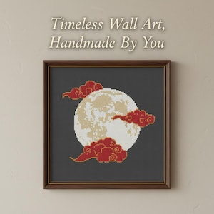 May include: A square framed cross-stitch embroidery featuring a large, textured white moon centered on a dark gray background, accented by stylized red clouds. Above the frame, the text reads: Timeless Wall Art, Handmade By You.