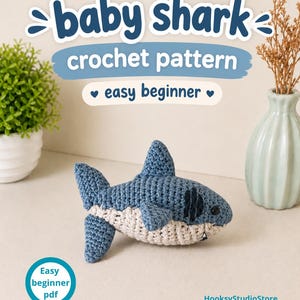 May include: A blue and cream crocheted shark toy with dark eyes and gills. The text reads: baby shark crochet pattern easy beginner. A circular badge says: Easy beginner pdf. The store name HooksyStudioStore is printed in the bottom right corner.