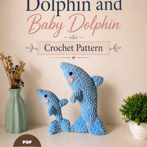 May include: A crochet pattern titled Dolphin and Baby Dolphin featuring two blue plush dolphin toys with pink cheeks and black eyes. The text reads Dolphin and Baby Dolphin Crochet Pattern and PDF PATTEFRN ONLY. The brand is HooksyStudioStore.